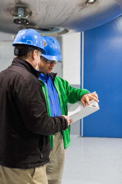 Two men in hard hats looking at binder